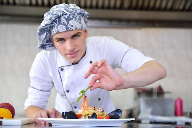 Красивый шеф-повар, одетый в белую форму, украшает салат из макарон и рыбу из морепродуктов на современной кухне