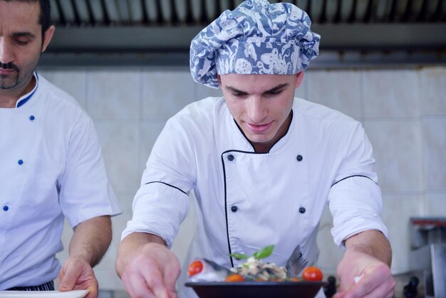 Handsome chef dressed in white uniform decorating pasta salad and seafood fish in modern kitchen