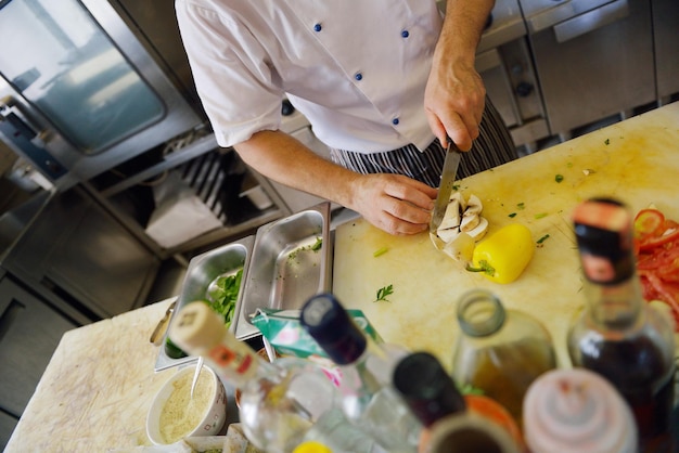 Handsome chef dressed in white uniform decorating pasta salad and seafood fish in modern kitchen