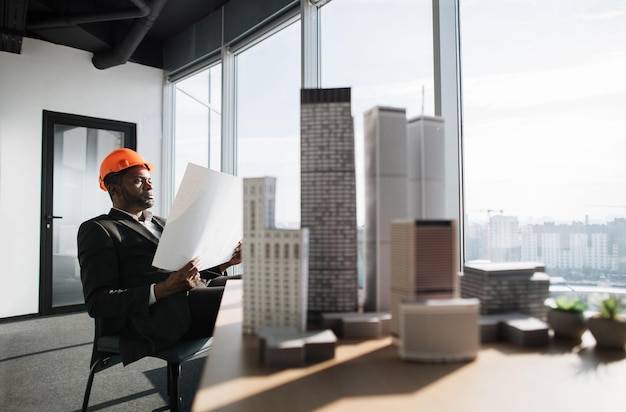 Handsome chief architect man in business suit and protective helmet holding blueprint