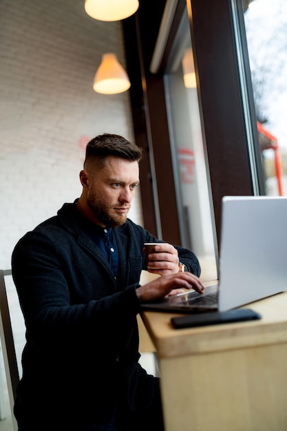 一杯のコーヒーで働くハンサムな自信を持ってビジネスマン。カフェで座っている若い成功した男。