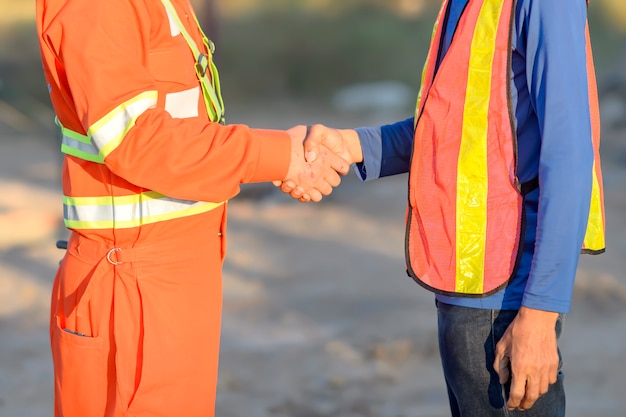 Handsome construction workers in protective helmets and vests are shaking hands while working in the office center