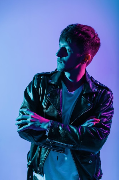 Handsome cool young man model with hairstyle in casual outwear with fashion leather jacket poses in studio with colorful future neon-pink lights. colored portrait of trendy guy