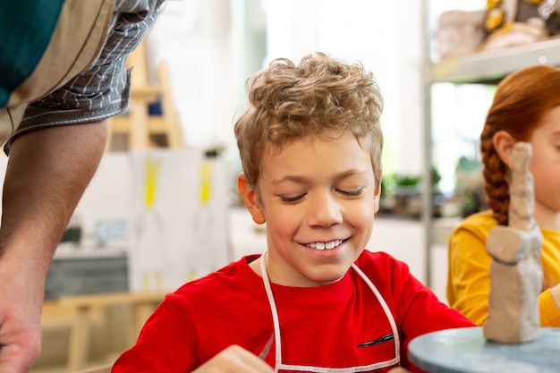 Bel ragazzo riccio sorridente mentre si sente bene alla scuola d'arte