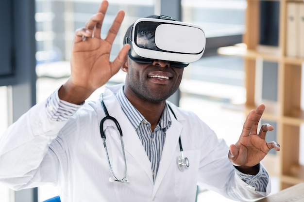 Handsome dark-skinned man keeping smile on face while wearing wearable gadget