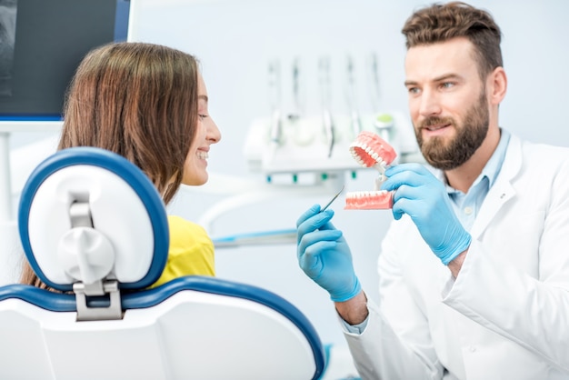 Handsome dentist consulting woman patient holding artificial jaw at the dental office