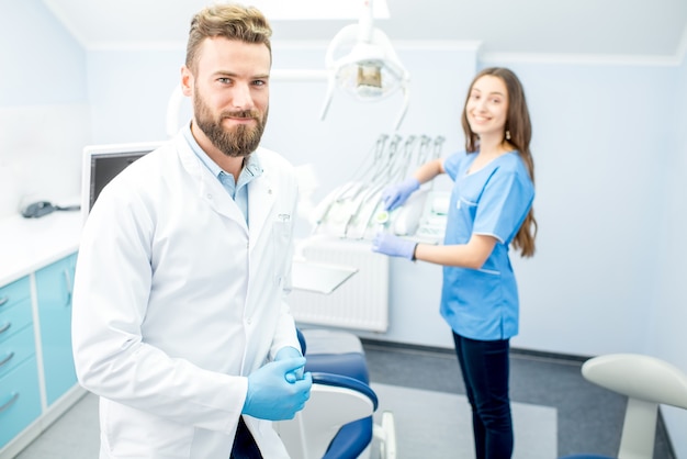 Photo handsome dentist with young female assistant in uniform prepairing for the job at the dental office