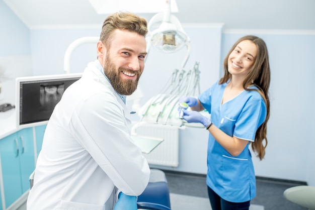 Handsome dentist with young female assistant in uniform prepairing for the job at the dental office