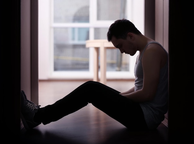 Handsome depressed man sitting on floor at home