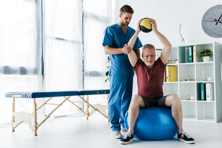 Photo handsome doctor standing near mature man exercising on fitness ball