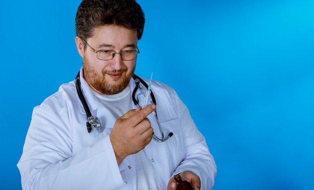 Handsome doctor wearing his uniform, holding injection by his both hands and smiling,