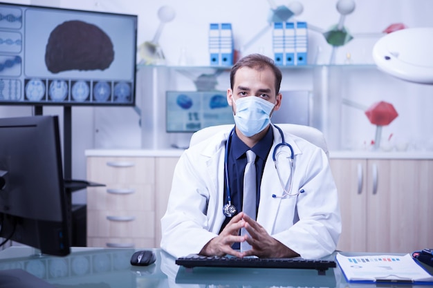 Handsome doctor wearking a mask against germs in the cabinet clinic. Medic following clinic protocol.