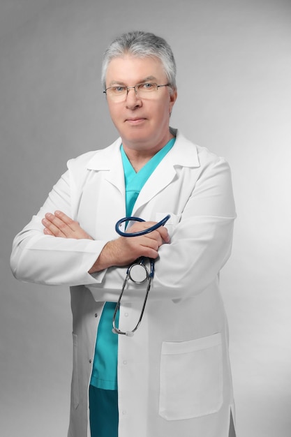 Foto un bel medico con le braccia incrociate in piedi su sfondo grigio