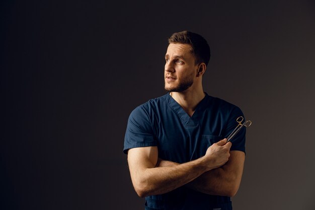 Handsome doctor with surgical scissors. Confident man holding medical equipment in hands and smiling.