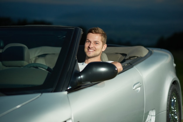 Handsome driver of silver cabriolet smiling.