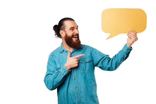 Handsome ecstatic bearded hipster man is pointing at a yellow speech bubble