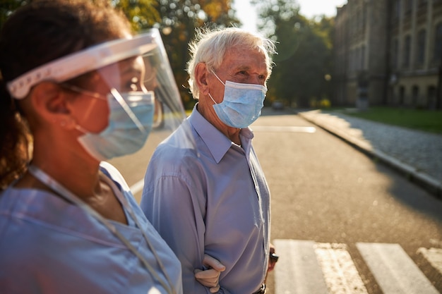 Photo handsome elderly man in protective mask spending time with medicine worker in the city