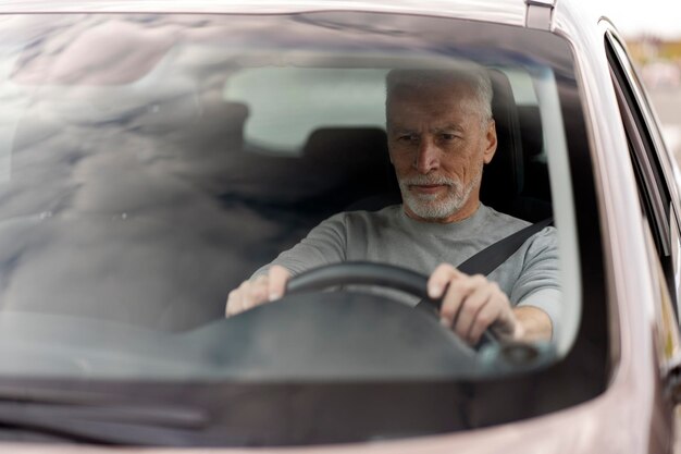 Фото Красивый пожилой мужчина кладет руки на руль за рулем автомобиля ставка на сиденье и безопасность вождения