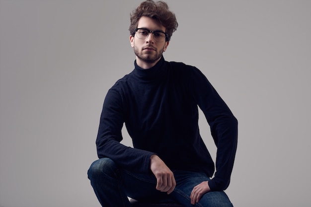 Handsome elegant man with curly hair wearing black turtleneck and glasses