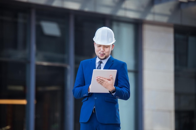 handsome engineer wearing suit and hard hat or white helmet on building background engineer using tablet for checking construction about modern building copy space for text