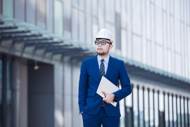 Handsome engineer wearing suit and hard hat or white helmet on building background Engineer using tablet for checking construction about modern building copy space for text