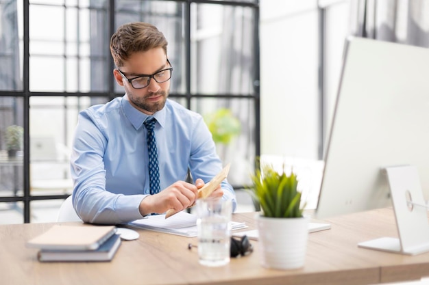 Handsome entrepreneur opening a padded envelope in a desktop at office