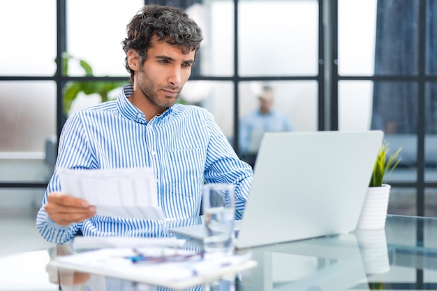 Handsome entrepreneur reading a letter from envelope in a desktop at office Collegue is on the background