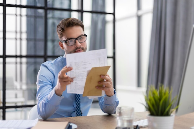 Handsome entrepreneur reading a letter from envelope in a desktop at office