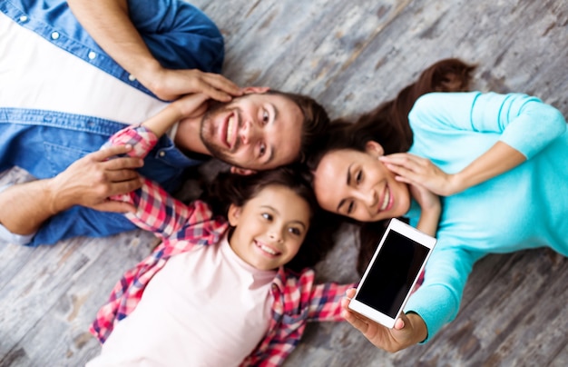 Handsome family of three people are laying on the floor, enjoying themselves and taking a selfie on their new smartphone