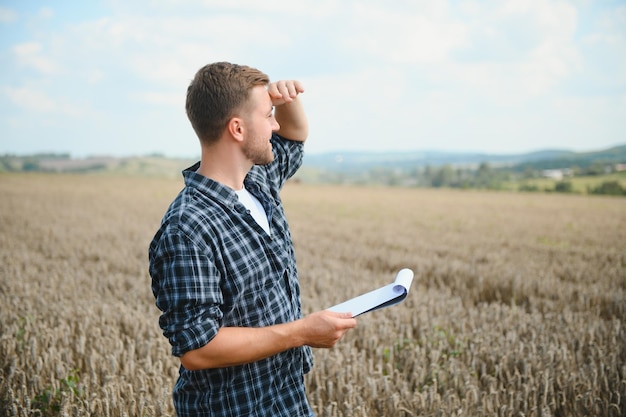 Handsome farmer with tablet standing in front of combine harvester during harvest in field