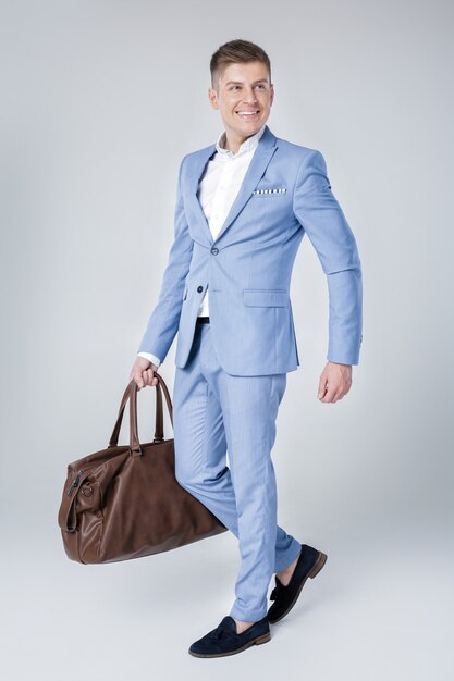 Handsome fashion young man in blue suit holding leather bag