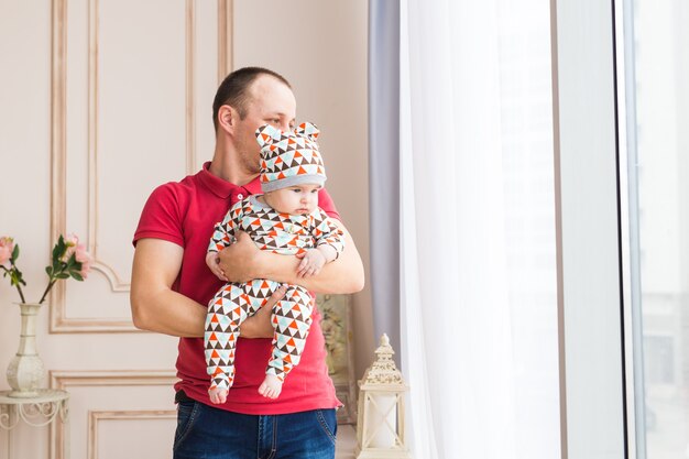 Handsome father holding a baby son against window