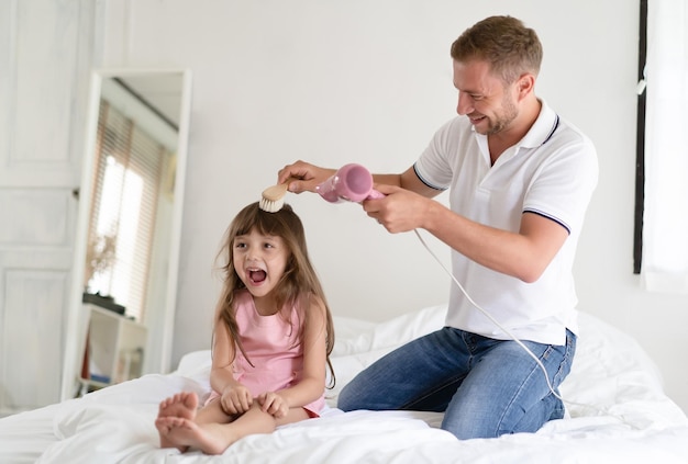 Handsome father takes care of her daughterFather dries hair with a blowdryer daughter of ittle girl