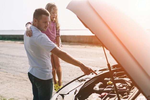 Foto padre bello che insegna a sua figlia in età scolare a cambiare l'olio del motore o a riparare l'automobile di famiglia.