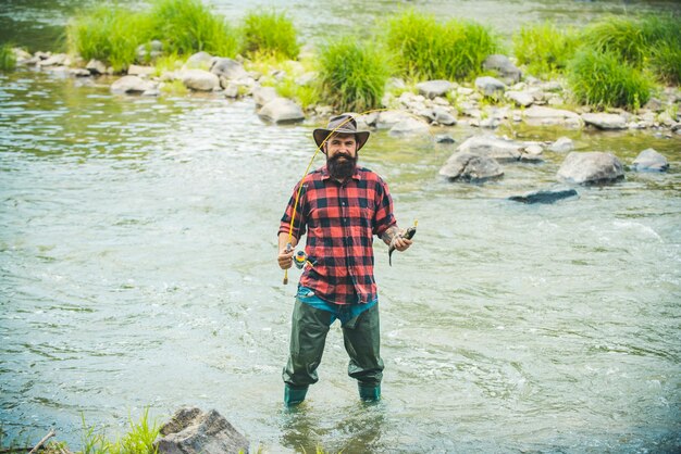 帽子と赤い市松模様のシャツを着たハンサムな漁師休日の釣りとして自然の背景をリラックスする男