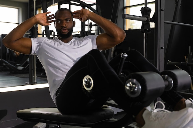 Handsome fit african man in sportwear doing crunches using a bench at gym