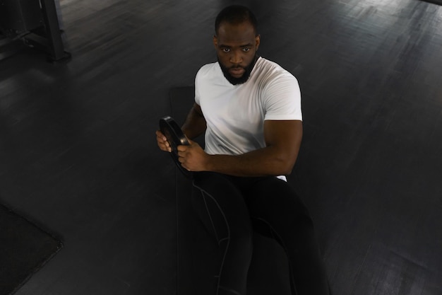 Photo handsome fit african man in sportwear doing crunches with damblebell in his hands at gym