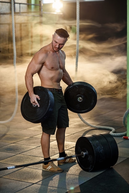 Handsome fit man doing exercise with weight plate in gym.