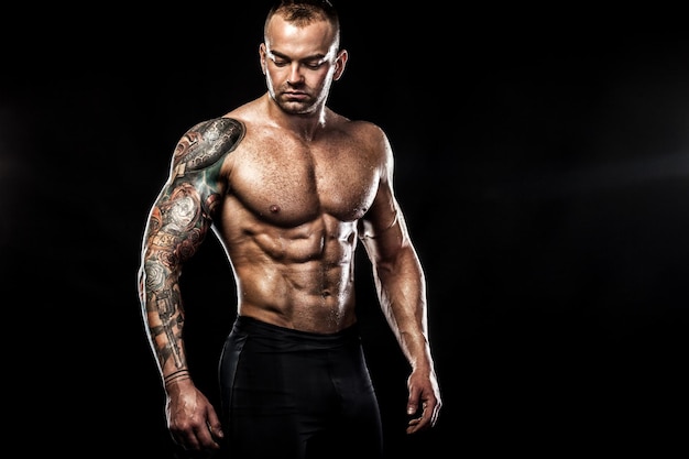 Handsome fit man posing wearing in jeans with tattoo Sport and fashion concept isolated on black background