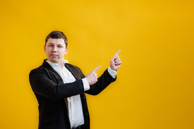 Handsome focused businessman wearing suit standing pointing fingers aside on mock up copy space on yellow studio background