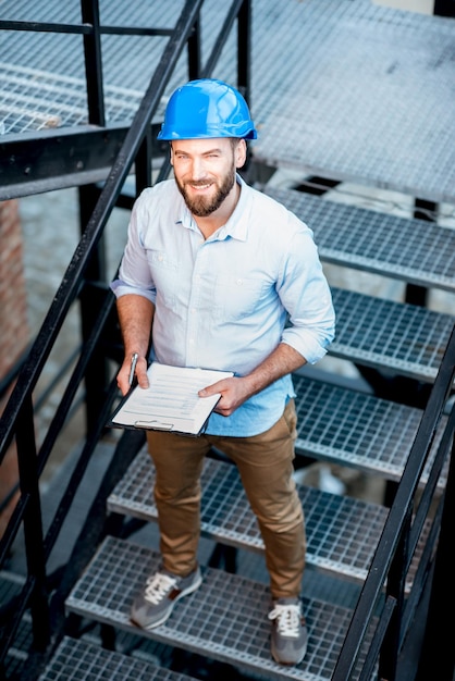 Handsome foreman or builder in helmet supervising structure standing on the new building stairs