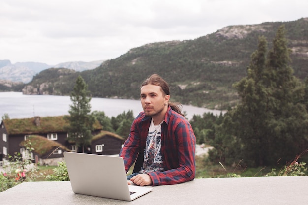 Handsome freelancer guy works on a laptop in nature on the\
background of mountains