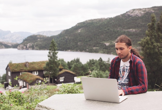 Handsome freelancer guy works on a laptop in nature on the\
background of mountains