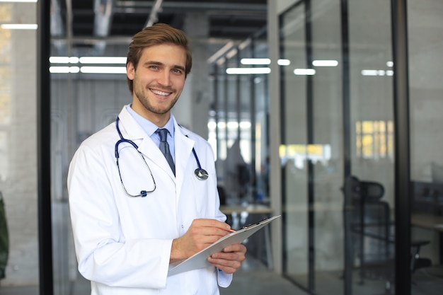 Handsome friendly young doctor on hospital corridor looking at camera, smiling.