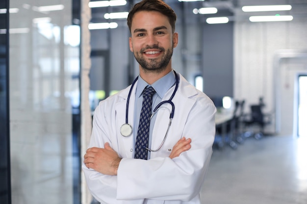 Handsome friendly young doctor on hospital corridor looking at camera, smiling.