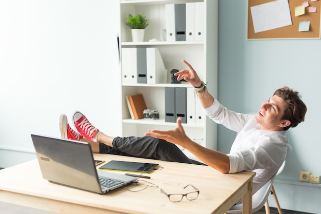 Handsome funny man in white shirt has a rest sitting at the table in office