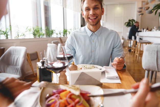 Handsome gentleman looking at lady and smiling while sitting at the table with delicious food and wine