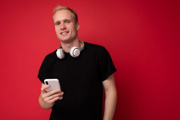 handsome good looking blonde young man wearing black t-shirt and white headphones standing