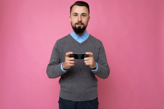 Handsome good looking brunet bearded young man wearing grey sweater and blue shirt isolated on pink
