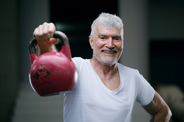 Handsome gray haired senior man with kettlebell weight Sport and health concept